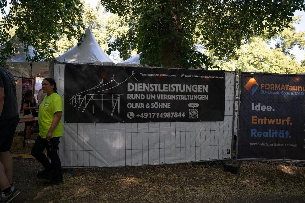 Werbebanner am Bauzaun mit der Zeichnung eines Zeltgerüsts und der Aufschrift „Dienstleistungen rund um Veranstaltungen, Oliva & Söhne“